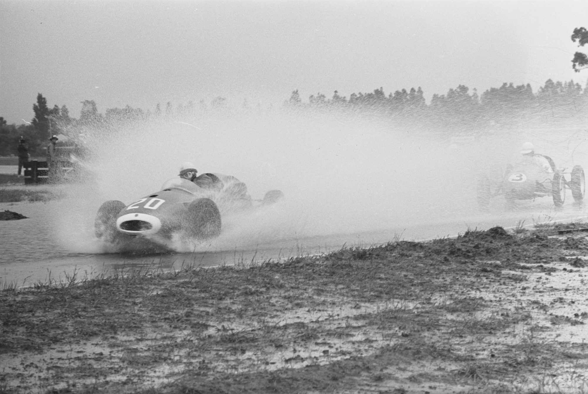 A grand prix car splashes through torrential rain and standing water